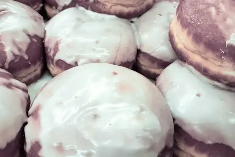 Pączki z fioletowym nadzieniem, polane błyszczącym lukrem z cukru pudru, kuszą swoim wyglądem.
