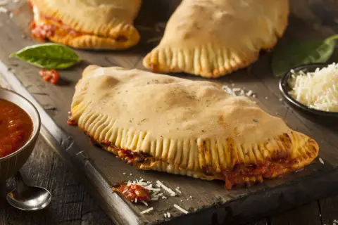 Pyszny calzone z kurczakiem, sos pomidorowy, starty ser i świeża bazylia na drewnianej desce.